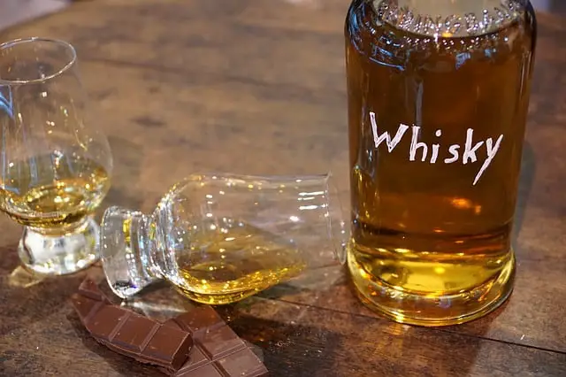 A bottle of homemade whiskey poured into two glasses