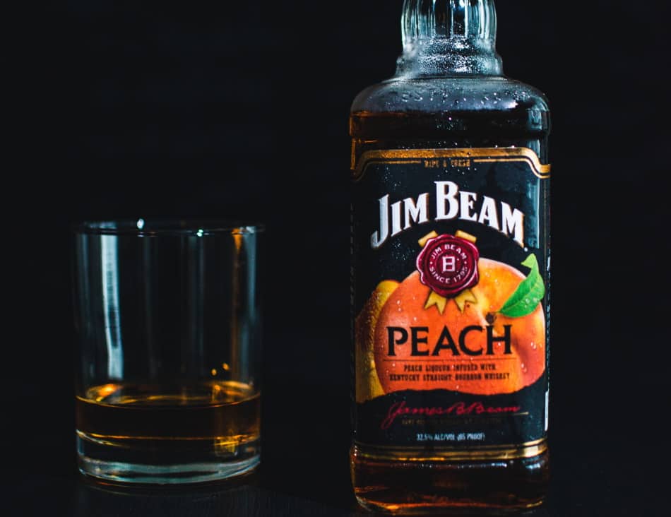 A bottle of Jim Beam Peach and a glass of whiskey