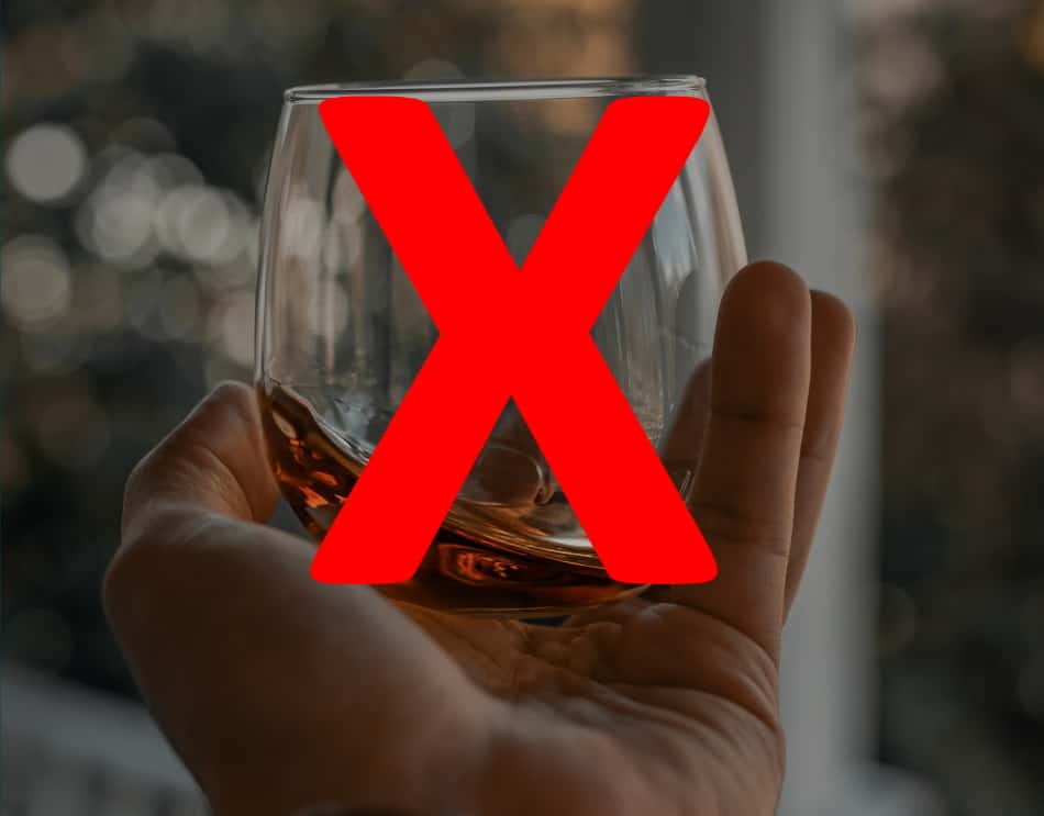 Someone holding a glass of whiskey close to get a good look at its color with a red X over it