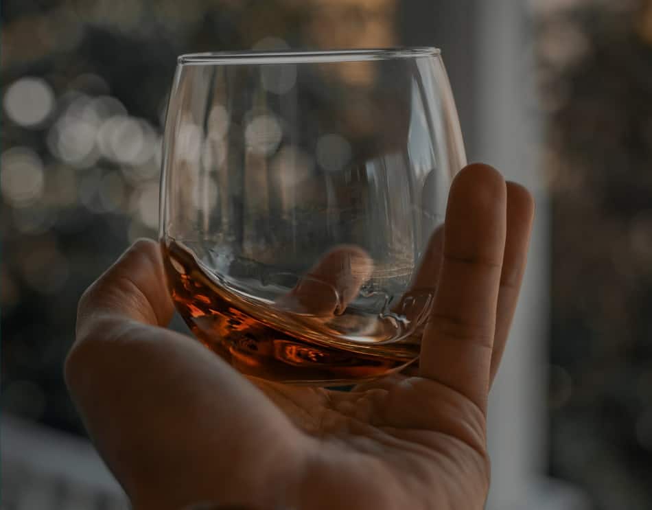 Someone holding a glass of whiskey close to get a good look at its color