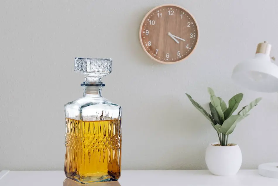 A decanter on a table in front of a clock on the wall
