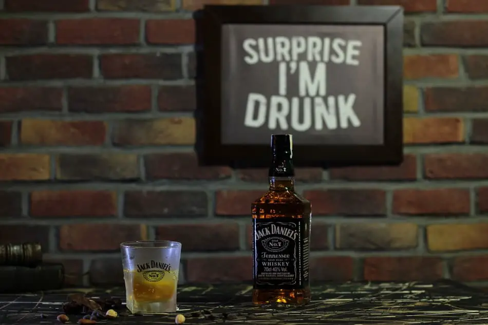A bottle and glass of Jack Daniel’s under a sign that says Surprise I’m Drunk