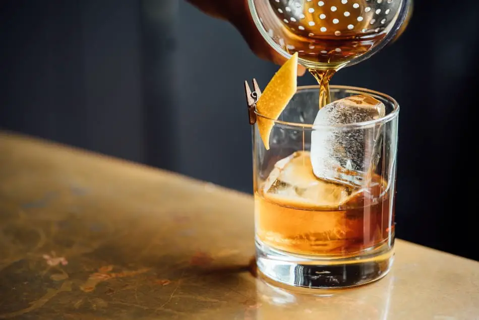 A cocktail being poured in to a whiskey glass