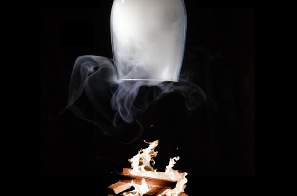 An upside smoking whiskey glass over burning ingredients