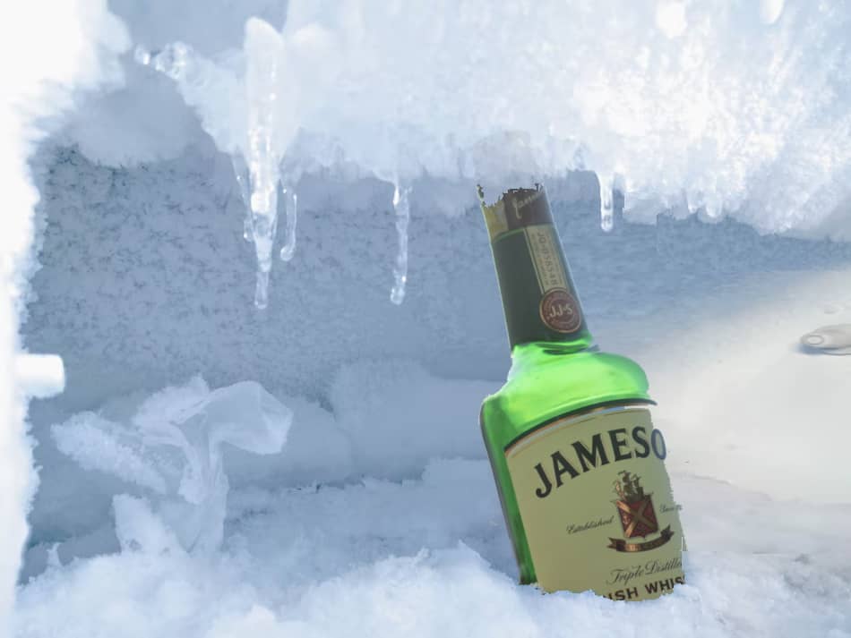A bottle of whiskey covered in ice in the freezer