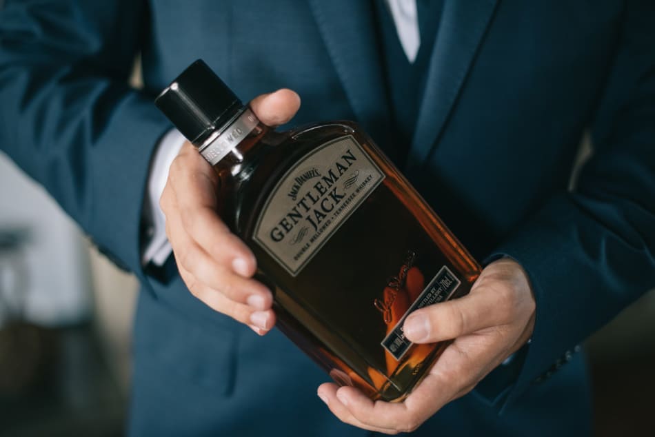 Man in a smart suit holding a bottle of bourbon